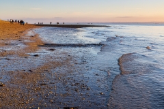 Gentle waves from the receding tide lap the gravel beach at Meon Beach as people take an afternoon stroll on a chill December day.